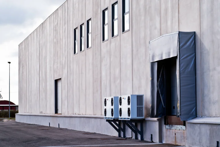 Fachada de galpão industrial de concreto com doca de carga e ar-condicionado externo, em dia nublado