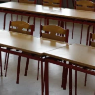 Carteiras e cadeiras de uma sala de aula vazia, iluminadas pela luz da manhã