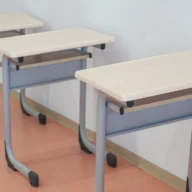 Carteiras escolares enfileiradas em sala de aula com luz natural