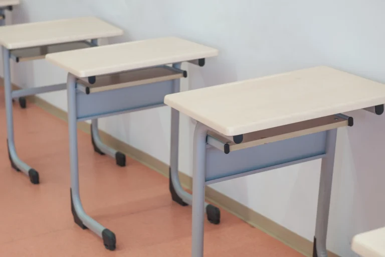Carteiras escolares enfileiradas em sala de aula com luz natural