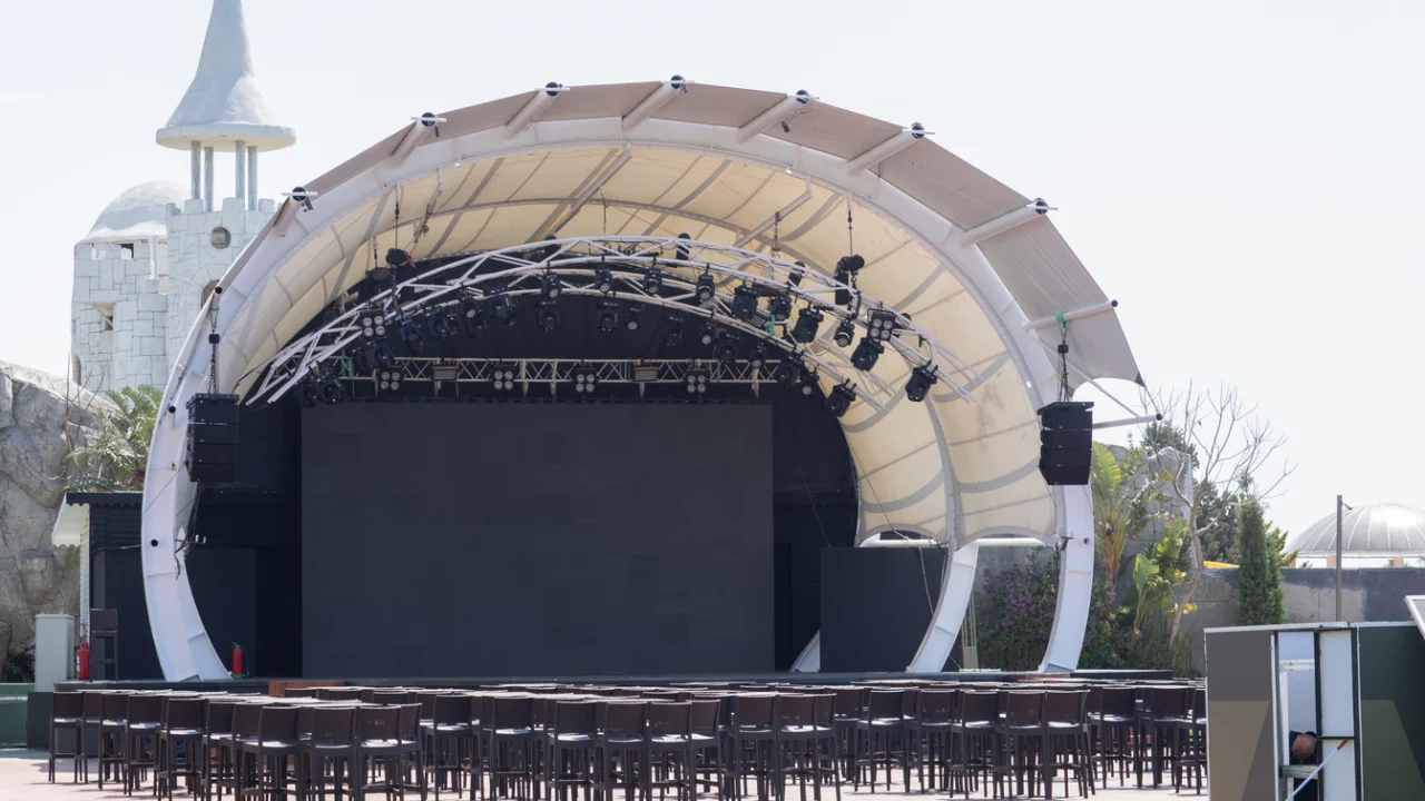 Palco de show montado ao ar livre, com estrutura metálica e refletores acesos à noite