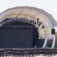 Palco de show montado ao ar livre, com estrutura metálica e refletores acesos à noite