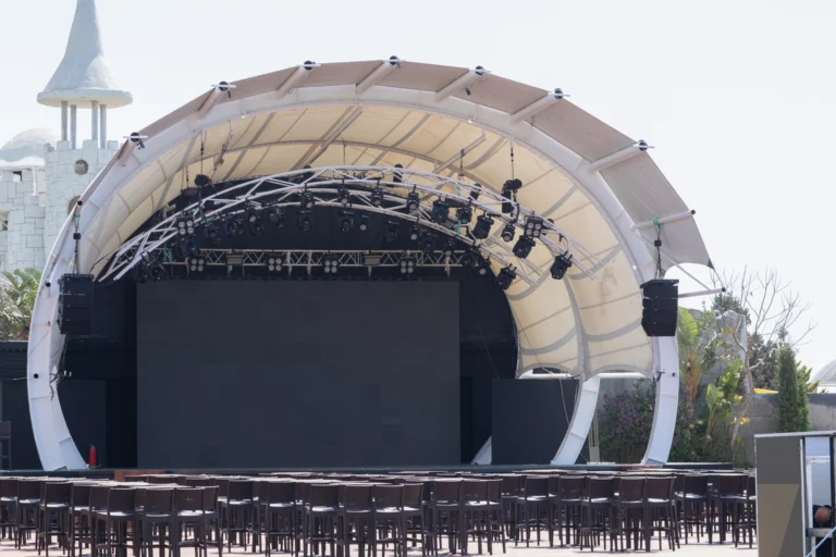 Palco de show montado ao ar livre, com estrutura metálica e refletores acesos à noite
