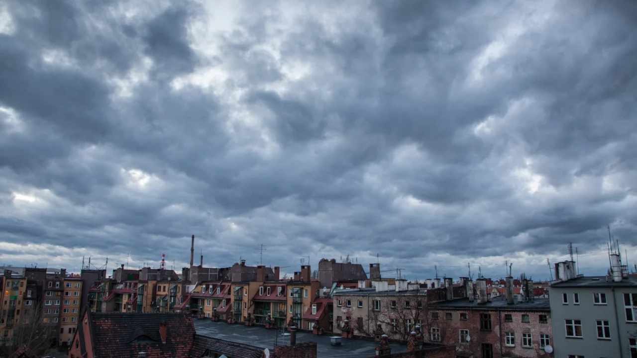Nuvens escuras de tempestade sobre a cidade, com ruas e telhados ao entardecer