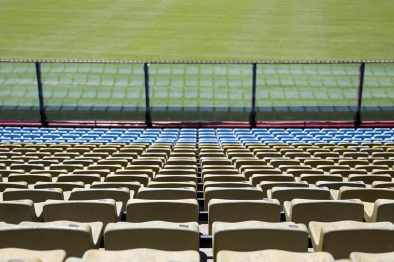 Arquibancadas vazias de estádio de futebol com cadeiras amarelas e azuis e o gramado ao fundo