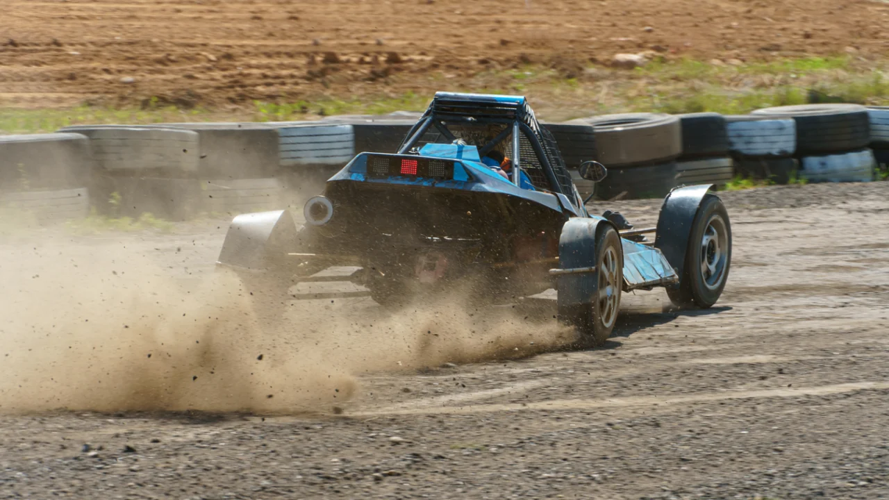 Carro de competição em pista de terra levantando poeira durante uma prova, com barreira de pneus ao fundo