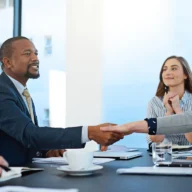 Duas pessoas apertando as mãos sobre uma mesa de reunião em sala clara