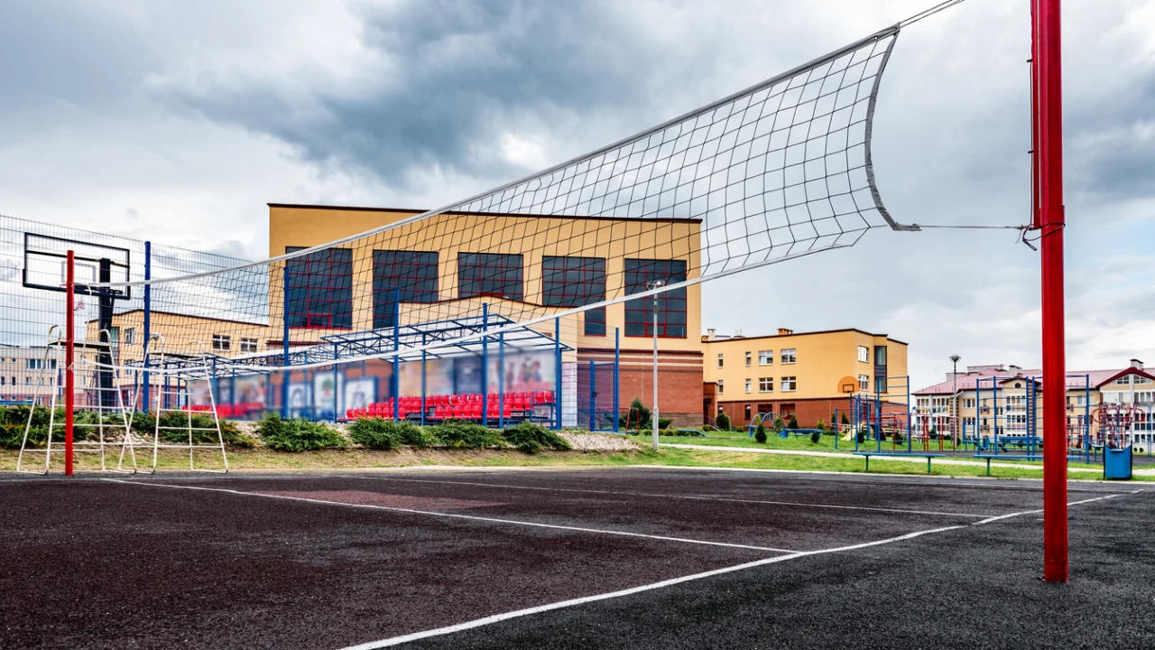Quadra esportiva externa de escola pública, com rede e cesta de basquete, ao lado do prédio escolar