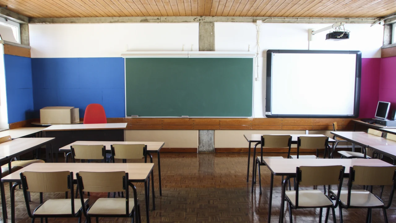 Sala de aula de escola pública com carteiras, quadro-negro e tela de projeção, sem alunos