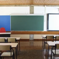 Sala de aula de escola pública com carteiras, quadro-negro e tela de projeção, sem alunos