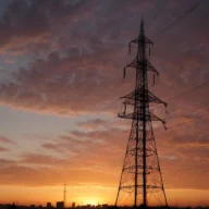 Torre metálica de transmissão de energia e cabos contra o céu no fim da tarde
