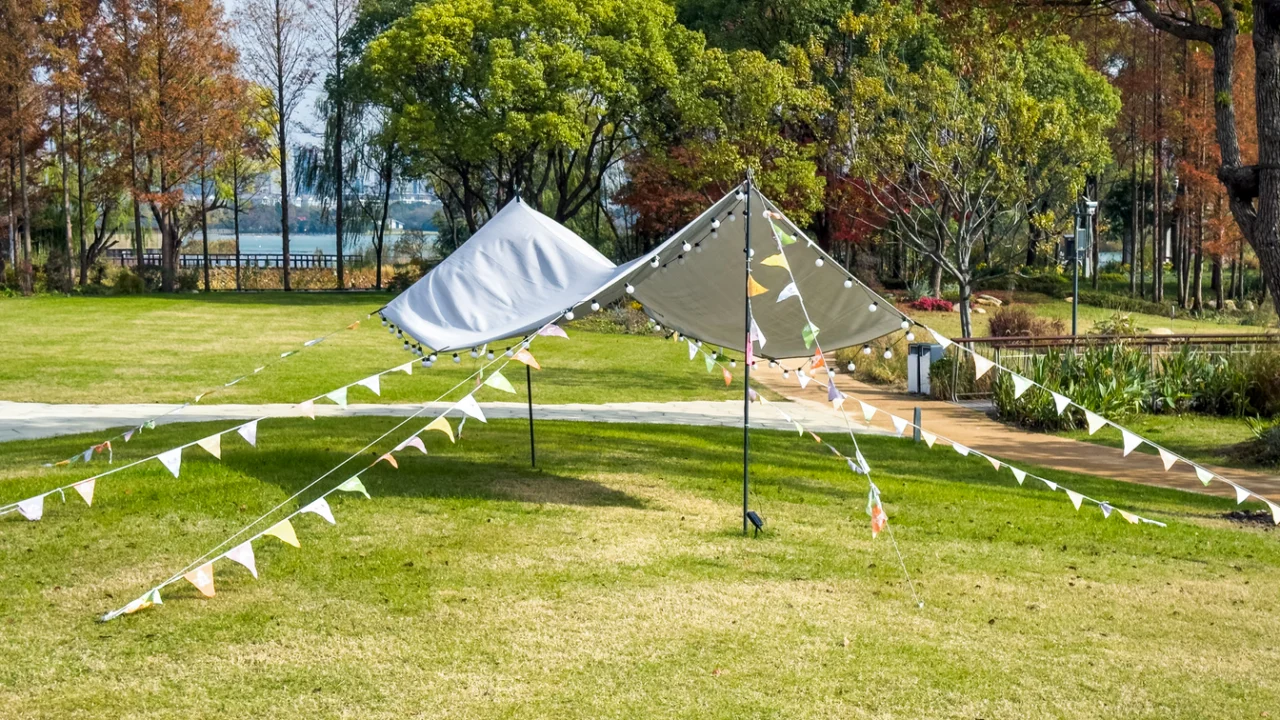 Tendas e bandeirinhas coloridas montadas em uma área verde de parque para evento ao ar livre