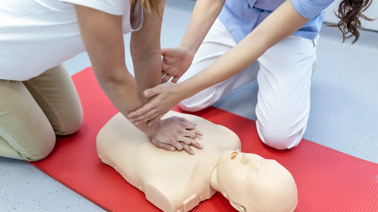 Mãos aplicando compressões em manequim de reanimação cardiopulmonar durante treinamento de primeiros socorros