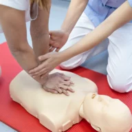Mãos aplicando compressões em manequim de reanimação cardiopulmonar durante treinamento de primeiros socorros