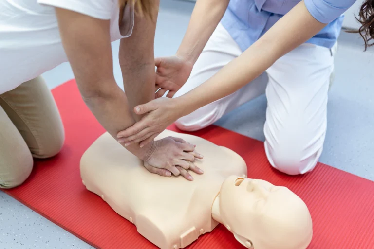 Mãos aplicando compressões em manequim de reanimação cardiopulmonar durante treinamento de primeiros socorros