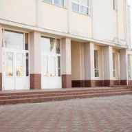 Entrada de prédio escolar público com escadaria de tijolos e portas de vidro, em manhã clara