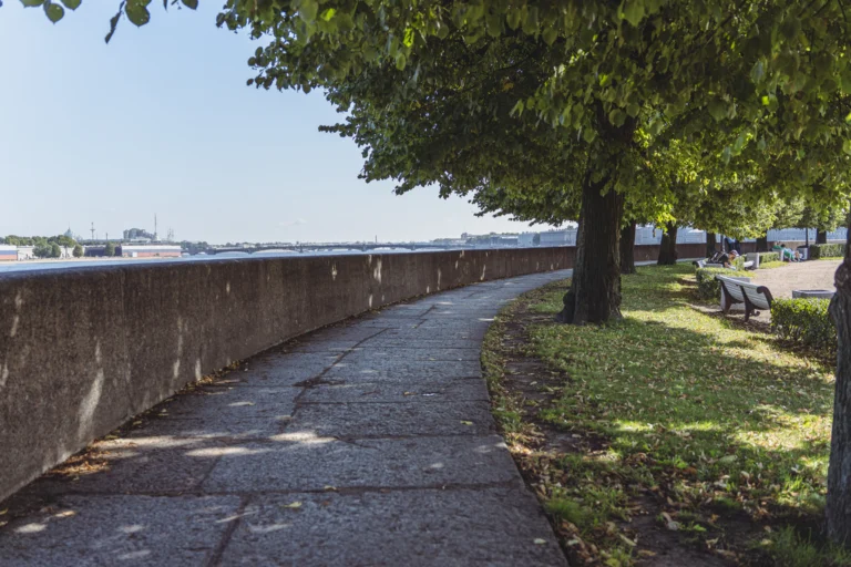 Calçadão arborizado às margens de rio, com mureta de concreto e bancos