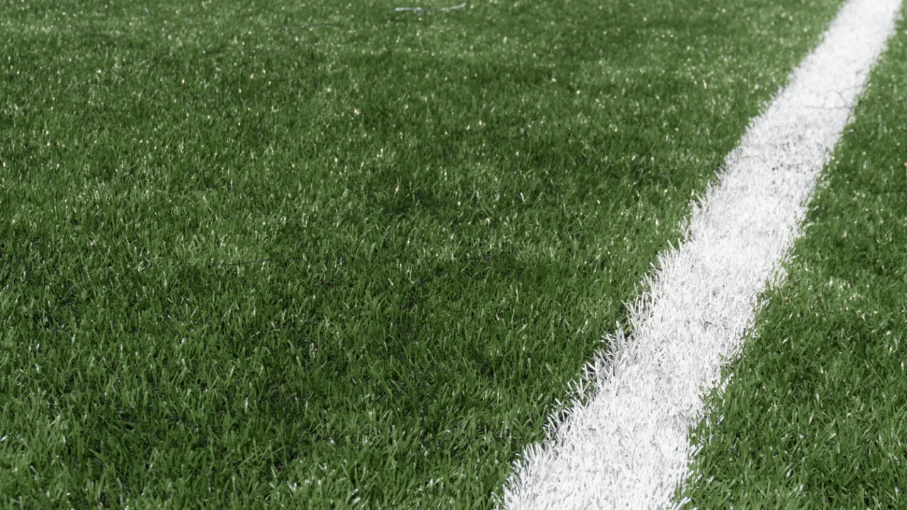 Gramado de campo de futebol com linha branca demarcatória sob luz de fim de tarde