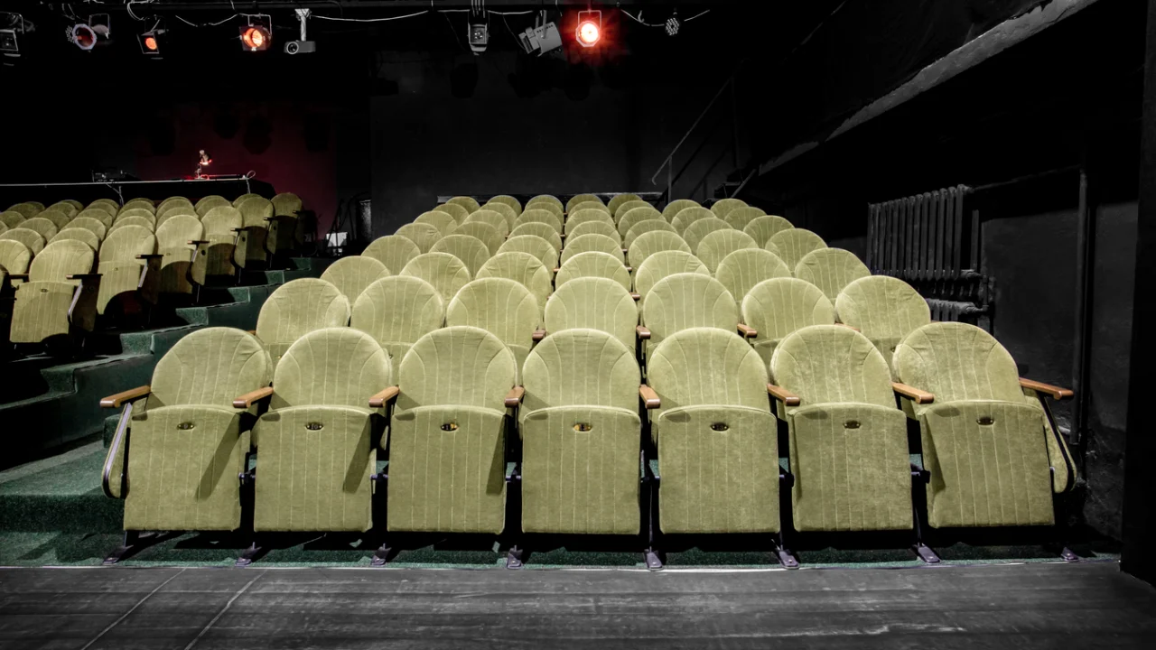 Poltronas de auditório de teatro municipal vazias sob luz de palco