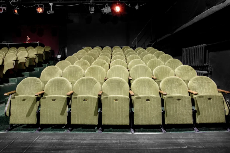Poltronas de auditório de teatro municipal vazias sob luz de palco