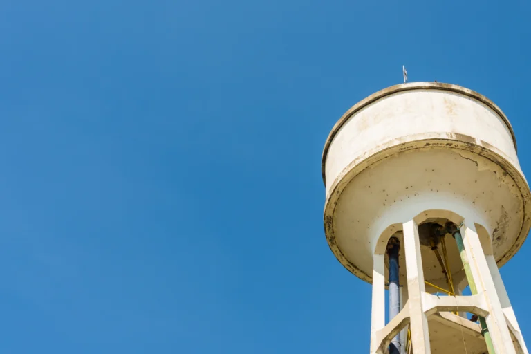Reservatório elevado de água de uma cidade, visto de baixo, com céu azul ao fundo