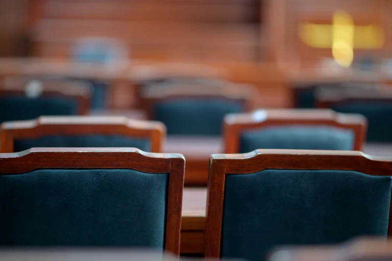 Cadeiras de madeira e mesa de uma sala de tribunal vazia, com luz natural