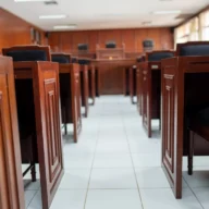 Sala de audiência com bancos e cadeiras de madeira enfileirados em um corredor central