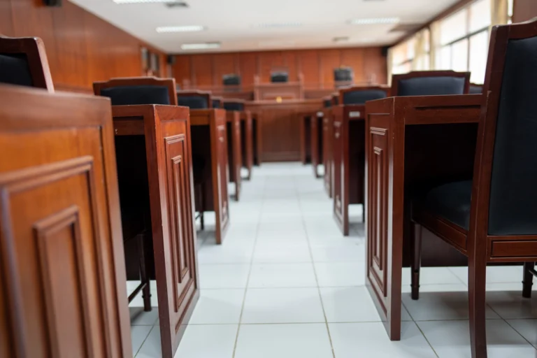 Sala de audiência com bancos e cadeiras de madeira enfileirados em um corredor central