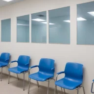 Sala de espera de unidade básica de saúde com cadeiras plásticas azuis e paredes claras