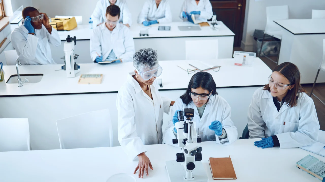 Laboratório de pesquisa universitário com bancadas, microscópio e estudantes de jaleco