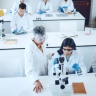 Laboratório de pesquisa universitário com bancadas, microscópio e estudantes de jaleco