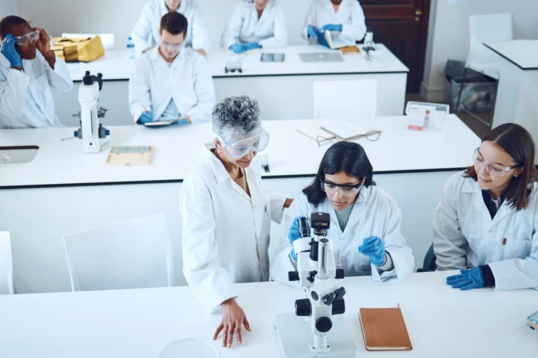 Laboratório de pesquisa universitário com bancadas, microscópio e estudantes de jaleco