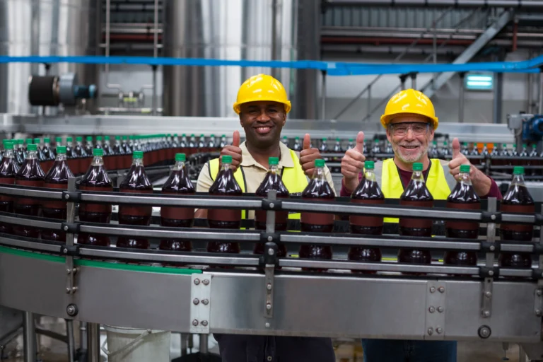 Dois trabalhadores de capacete e colete refletivo em linha de produção de bebidas em uma fábrica