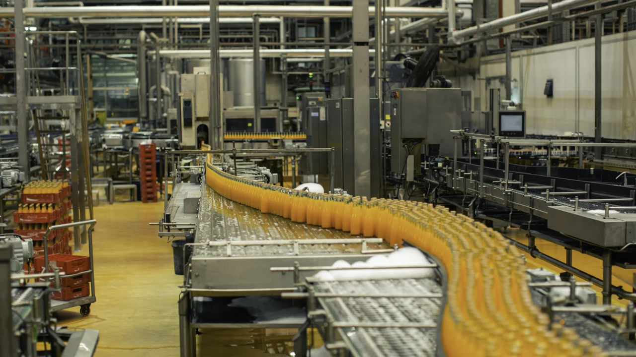 Linha de engarrafamento de sucos em indústria de bebidas, com esteira transportadora e trabalhadores de uniforme.