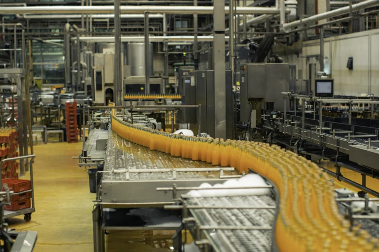 Linha de engarrafamento de sucos em indústria de bebidas, com esteira transportadora e trabalhadores de uniforme.